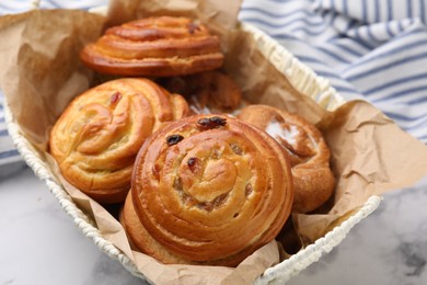 Delicious rolls with raisins and sugar powder in basket on white table, closeup. Sweet buns