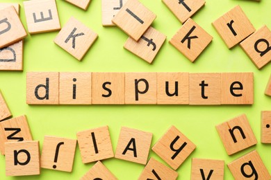 Photo of Word Dispute made with wooden cubes on light green background, flat lay
