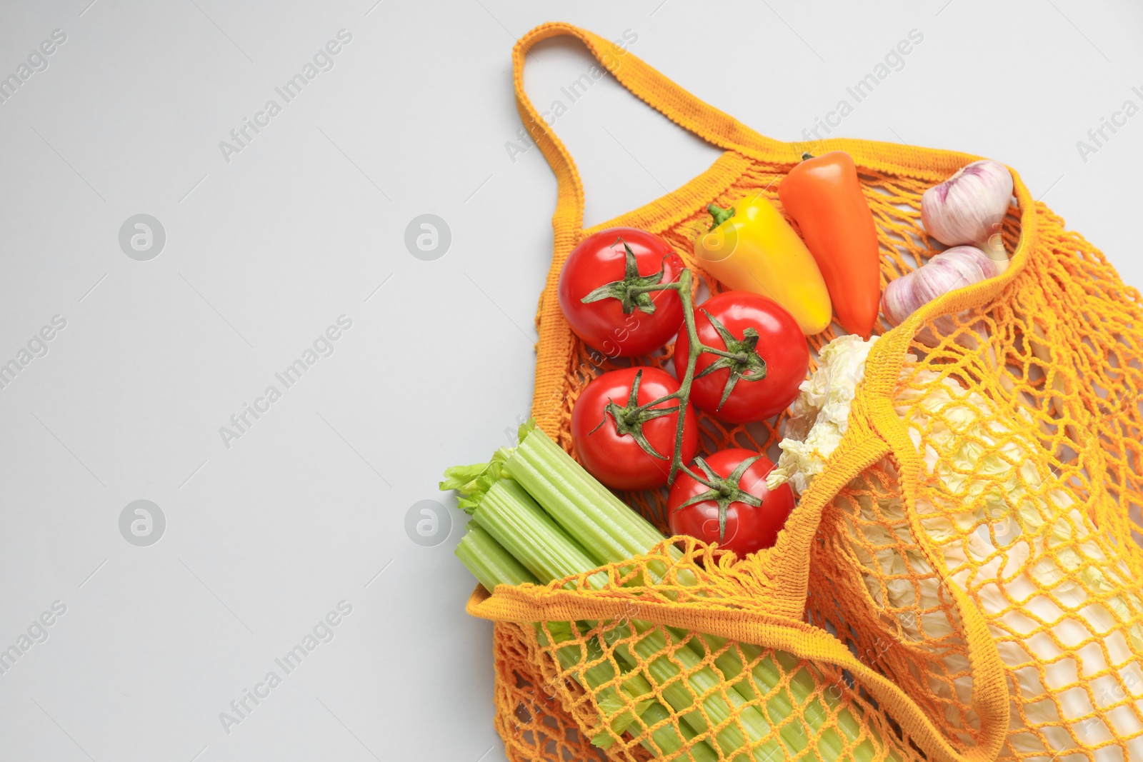 Photo of String bag with different vegetables on light grey background, top view. Space for text