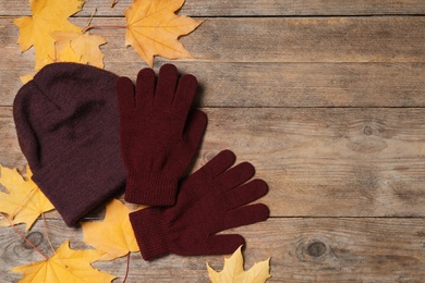 Stylish woolen gloves, hat and dry leaves on wooden table, flat lay. Space for text