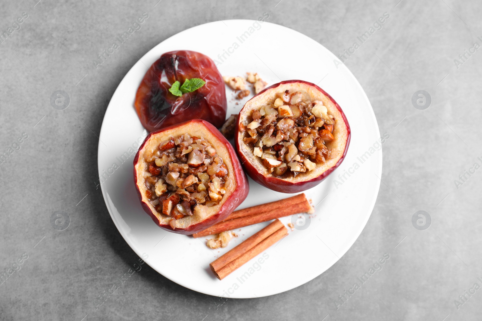 Photo of Tasty baked apples with nuts, honey, cinnamon sticks and mint on gray table, top view