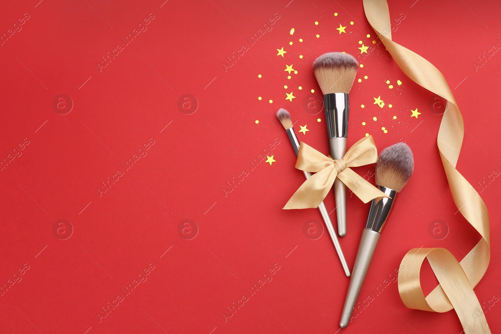 Photo of Different makeup brushes, ribbons and shiny confetti on red background, flat lay. Space for text