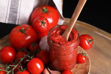 Photo of Jar of tasty tomato paste with spoon and ingredients on wooden table