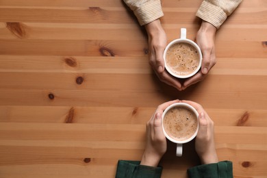 Women with cups of coffee at wooden table, top view. Space for text