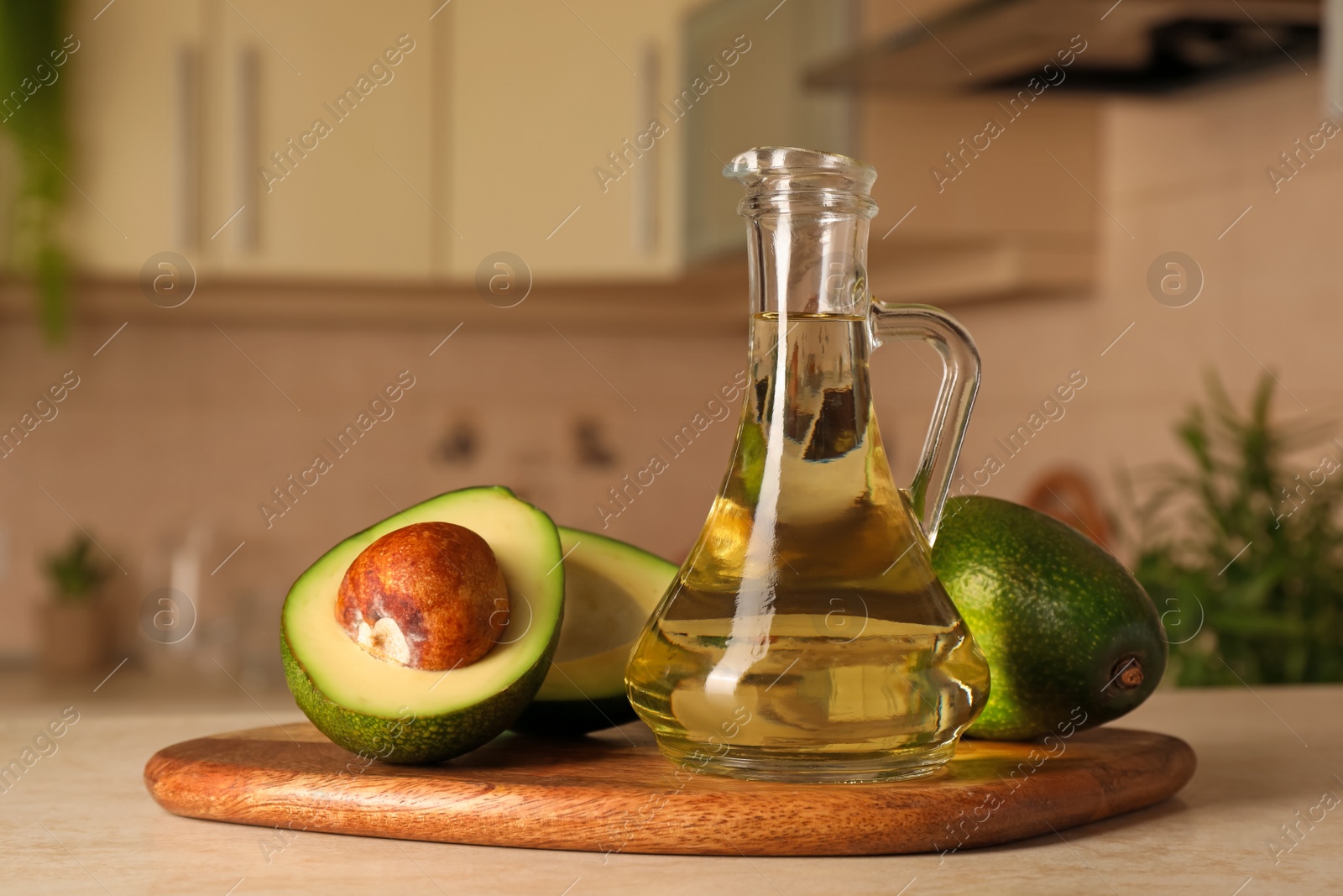 Photo of Fresh avocados and jug of cooking oil on beige marble table in kitchen