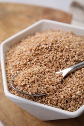 Photo of Dry wheat groats and spoon in bowl on table, closeup