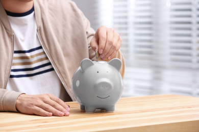 Man putting coin into piggy bank at wooden table, closeup