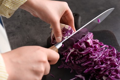 Woman cutting fresh red cabbage at black table, closeup