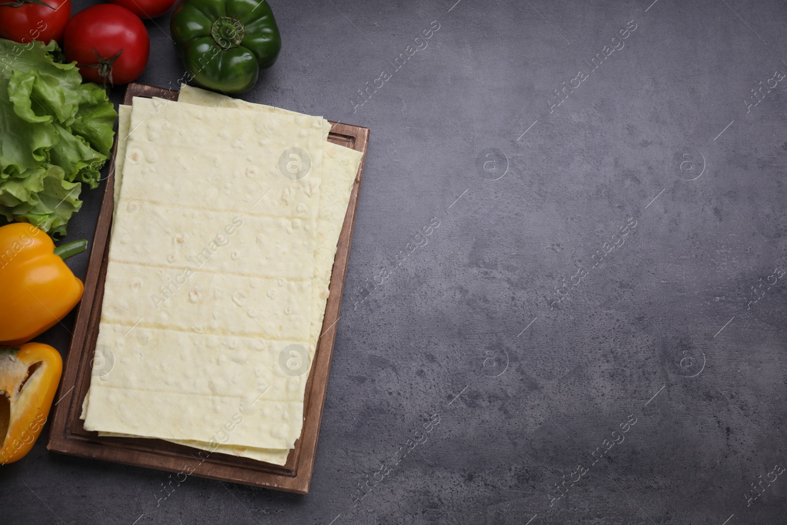 Photo of Delicious Armenian lavash and fresh vegetables on dark table, flat lay. Space for text