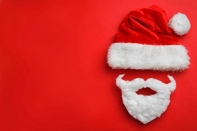 Photo of Santa Claus hat with white beard on red background, flat lay. Space for text