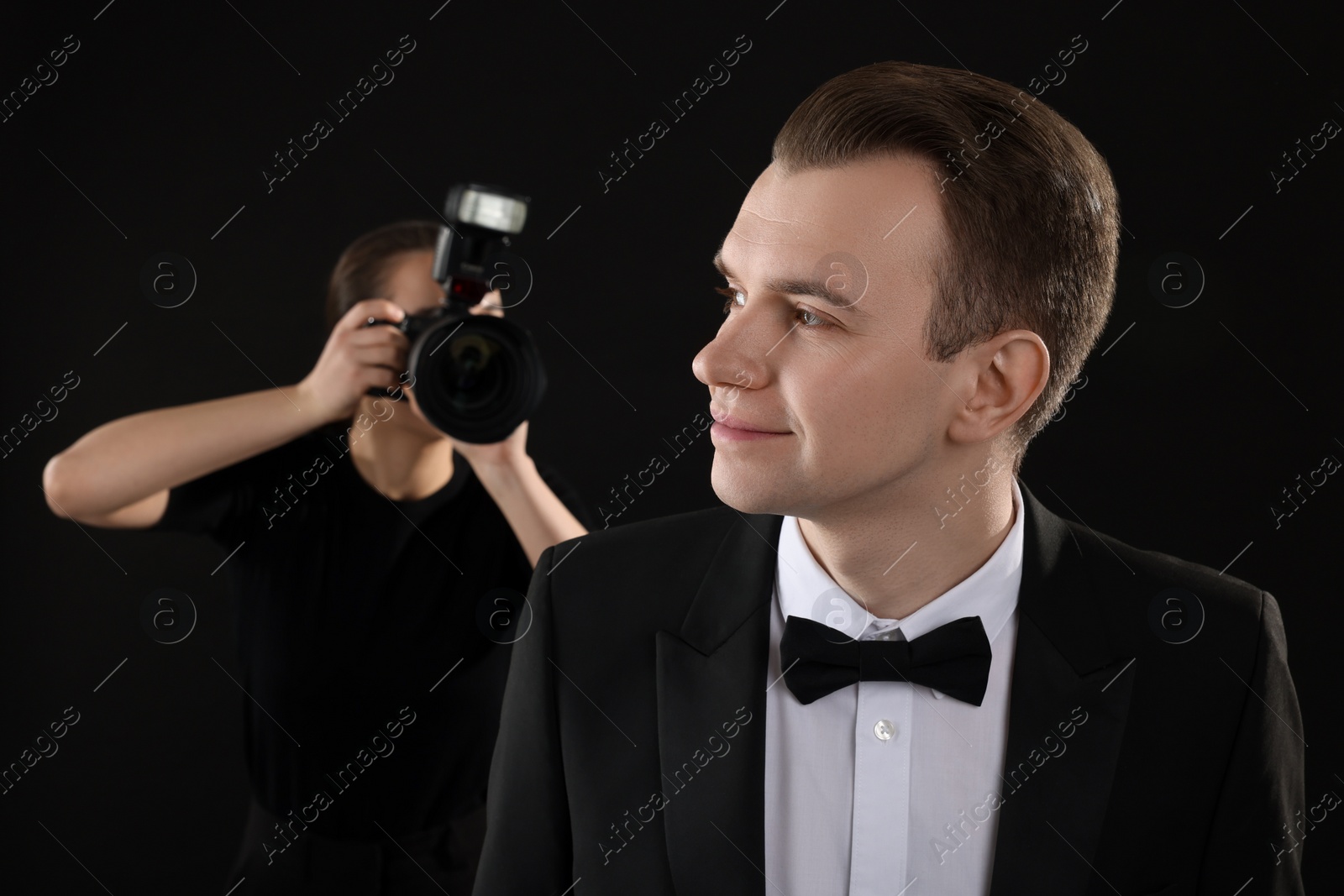 Photo of Professional photographer taking picture of man on black background, selective focus