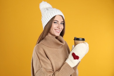 Happy beautiful woman with paper cup of mulled wine on yellow background