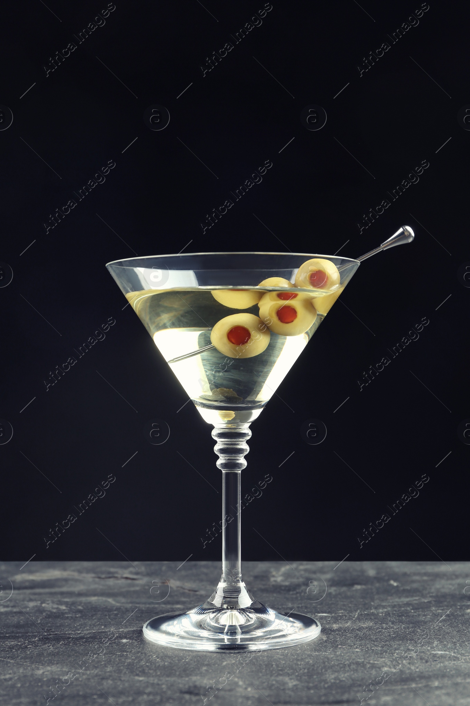 Photo of Martini cocktail with olives on grey table against dark background