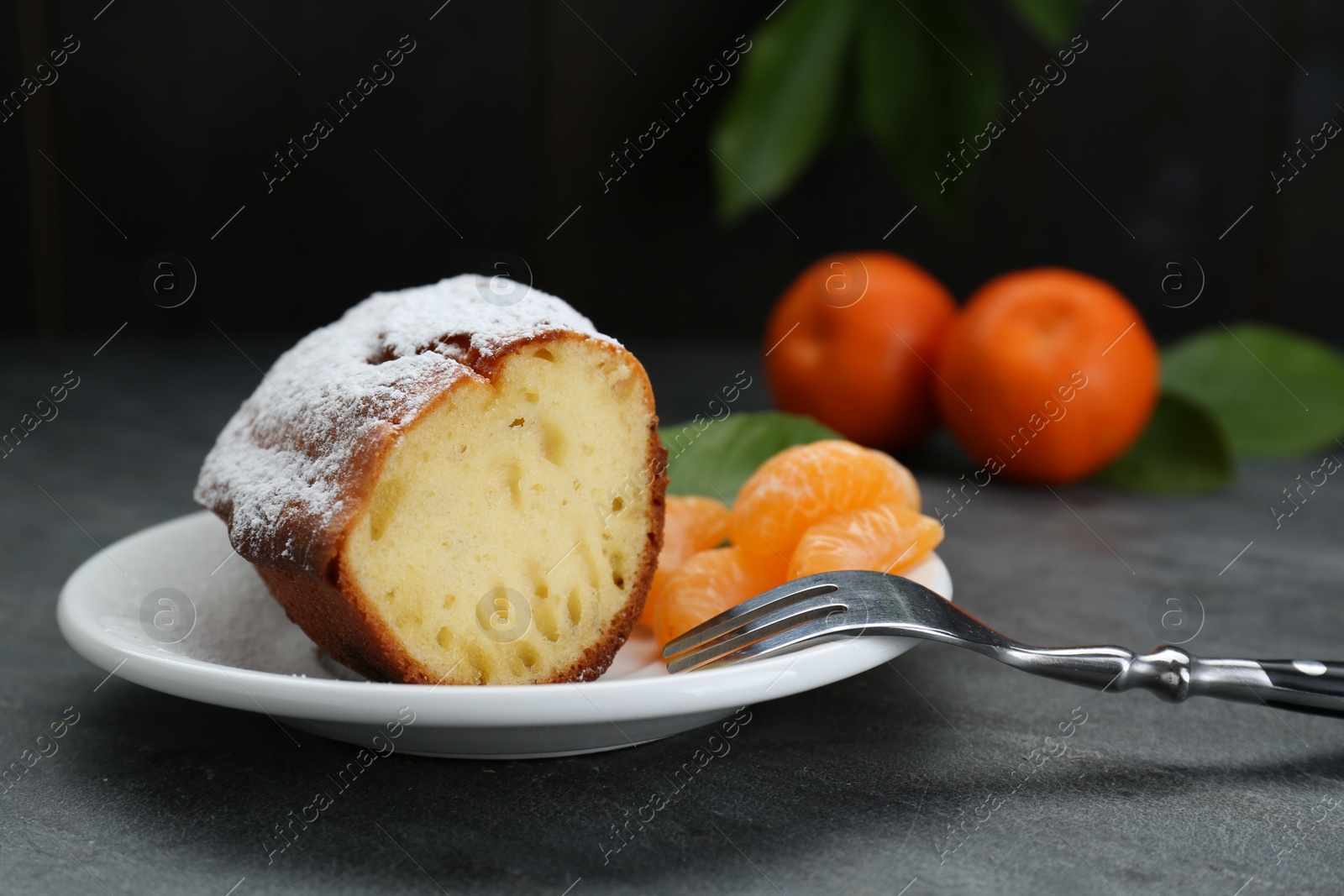 Photo of Piece of delicious homemade yogurt cake with powdered sugar and tangerines on gray table