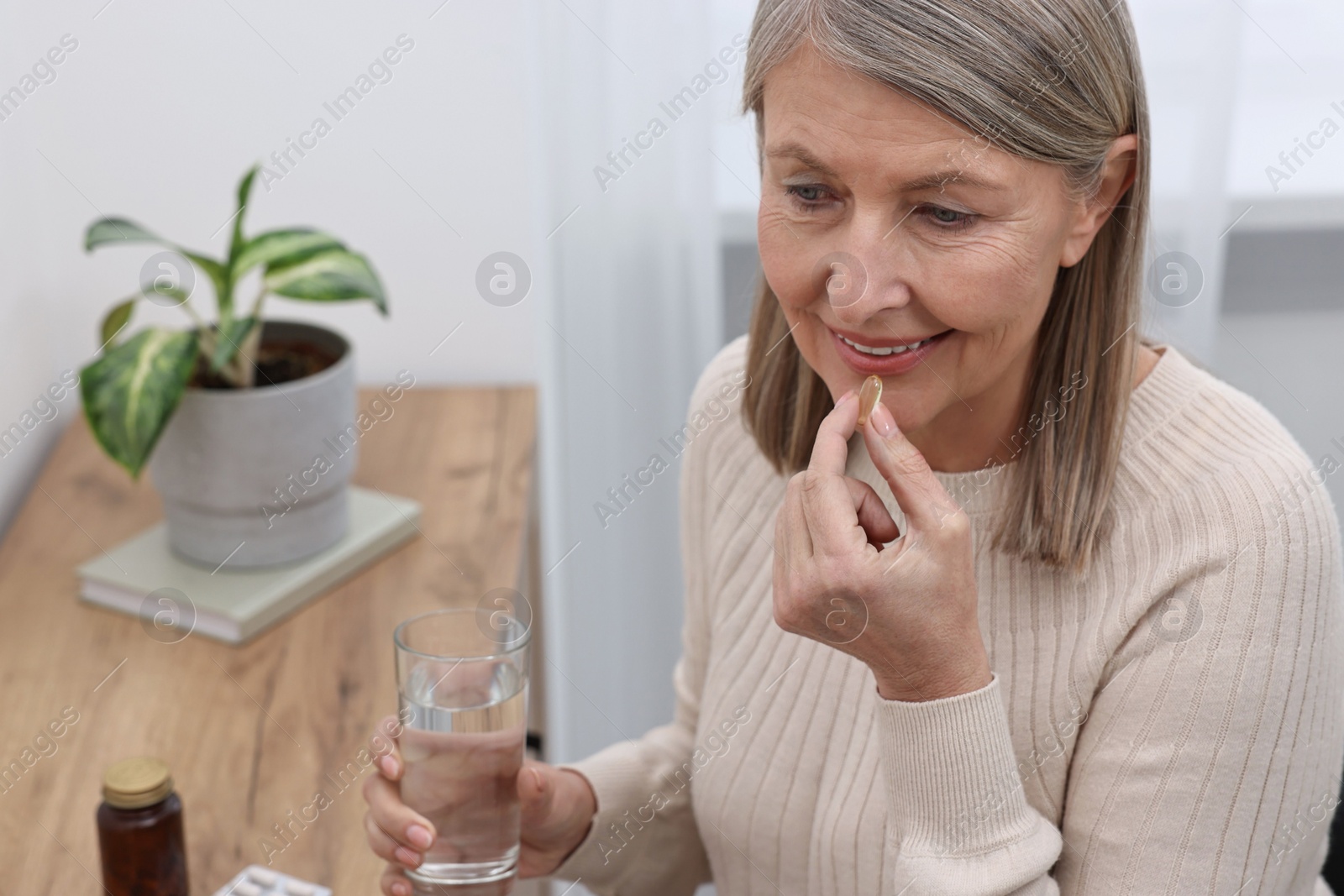 Photo of Beautiful woman taking vitamin pill at table indoors