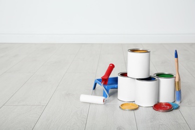 Photo of Cans of paint and decorator tools on wooden floor indoors. Space for text