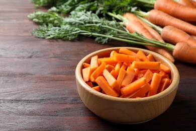 Photo of Cut carrot in bowl on brown wooden table, closeup