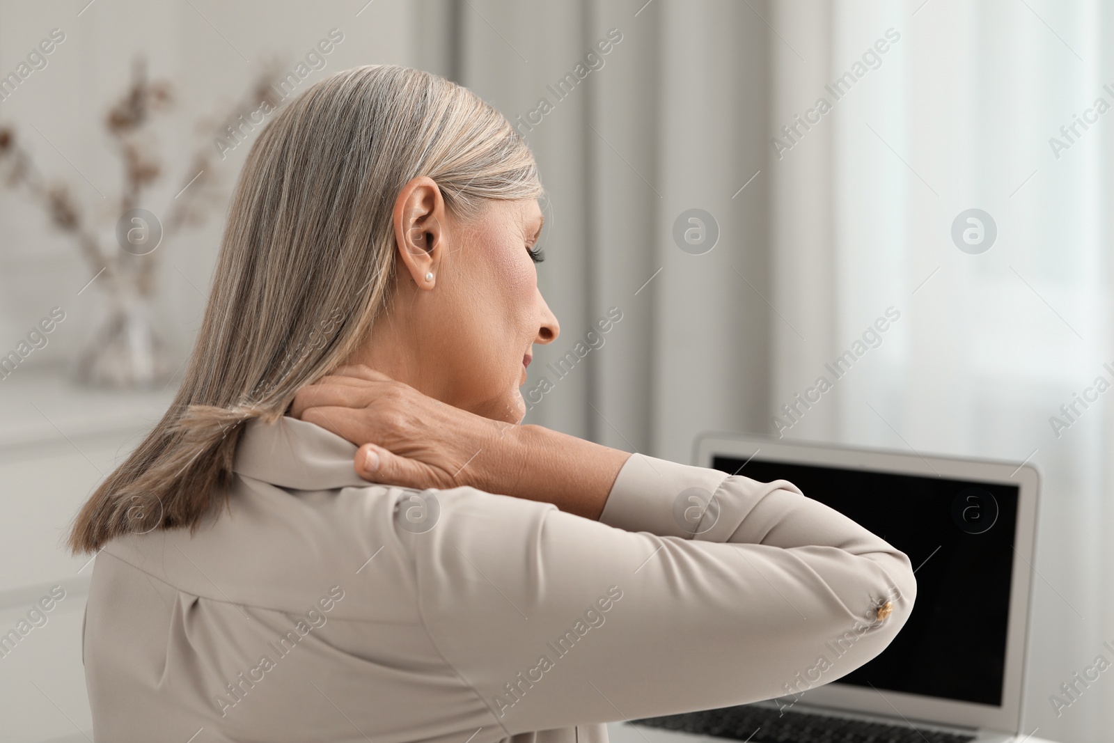 Photo of Woman suffering from neck pain at workplace in room