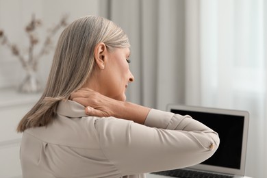 Woman suffering from neck pain at workplace in room