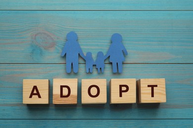 Photo of Family figure and word Adopt made of cubes on light blue wooden table