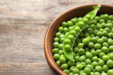 Bowl with green peas on wooden background, closeup