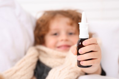 Photo of Cute little boy showing nasal spray on bed, focus on hand