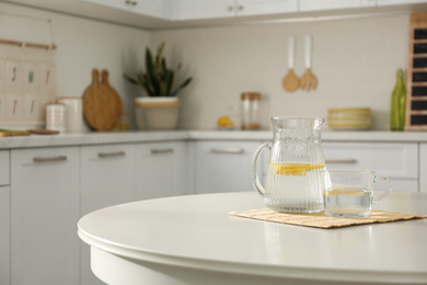 Photo of Fresh lemonade on white round table in kitchen. Stylish interior design