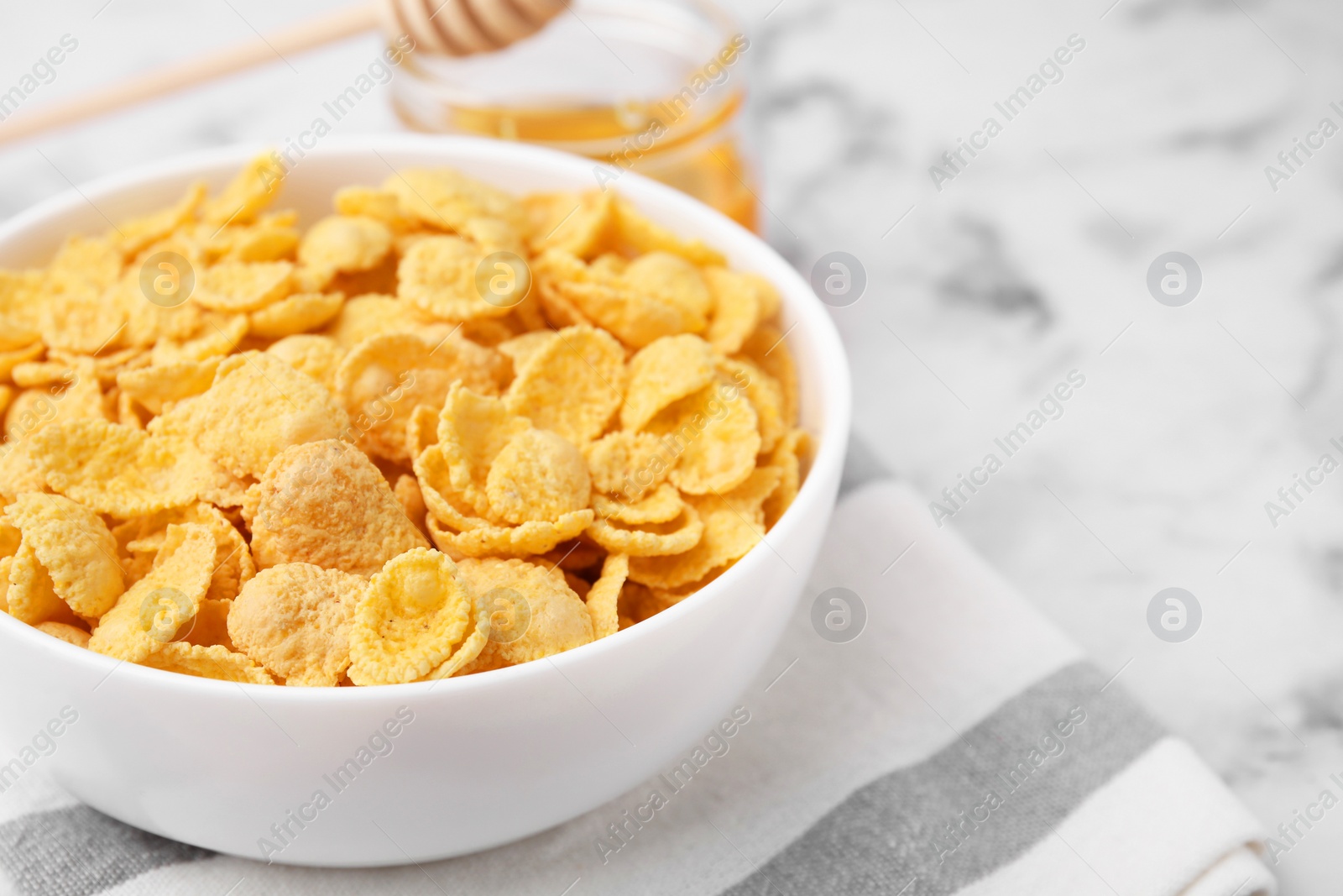 Photo of Breakfast cereal. Tasty crispy corn flakes in bowl on white marble table, closeup. Space for text