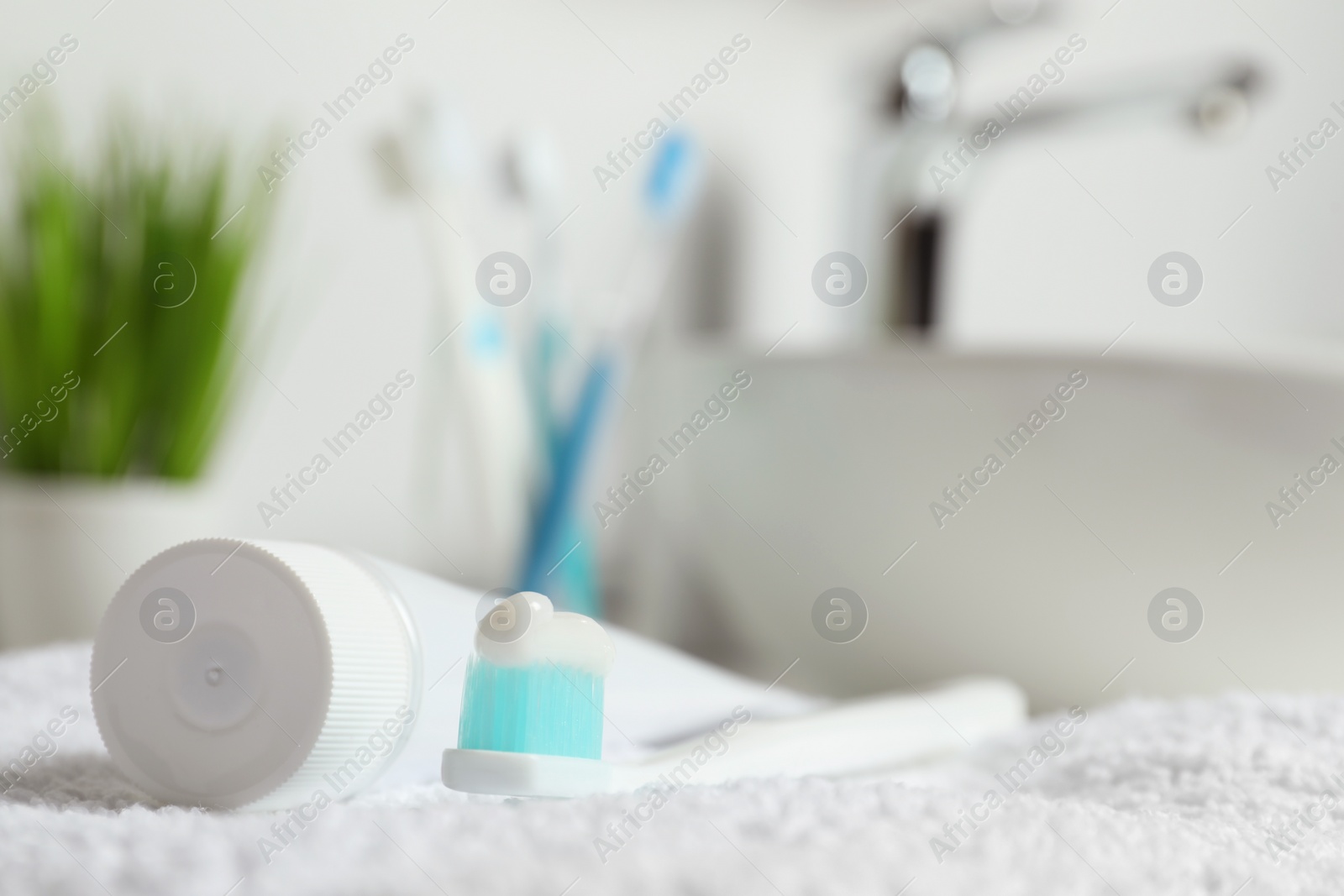 Photo of Plastic toothbrush with paste and tube on white towel in bathroom, closeup. Space for text