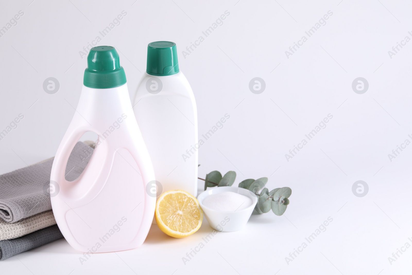 Photo of Bottles of cleaning product, brush, rags and lemon on light background