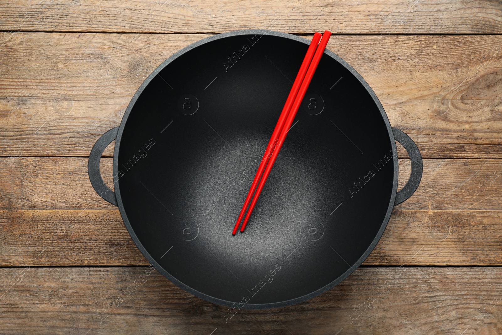 Photo of Empty iron wok with chopsticks on wooden table, top view