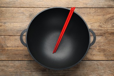 Photo of Empty iron wok with chopsticks on wooden table, top view