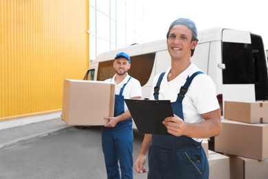 Male movers with box and clipboard near van outdoors