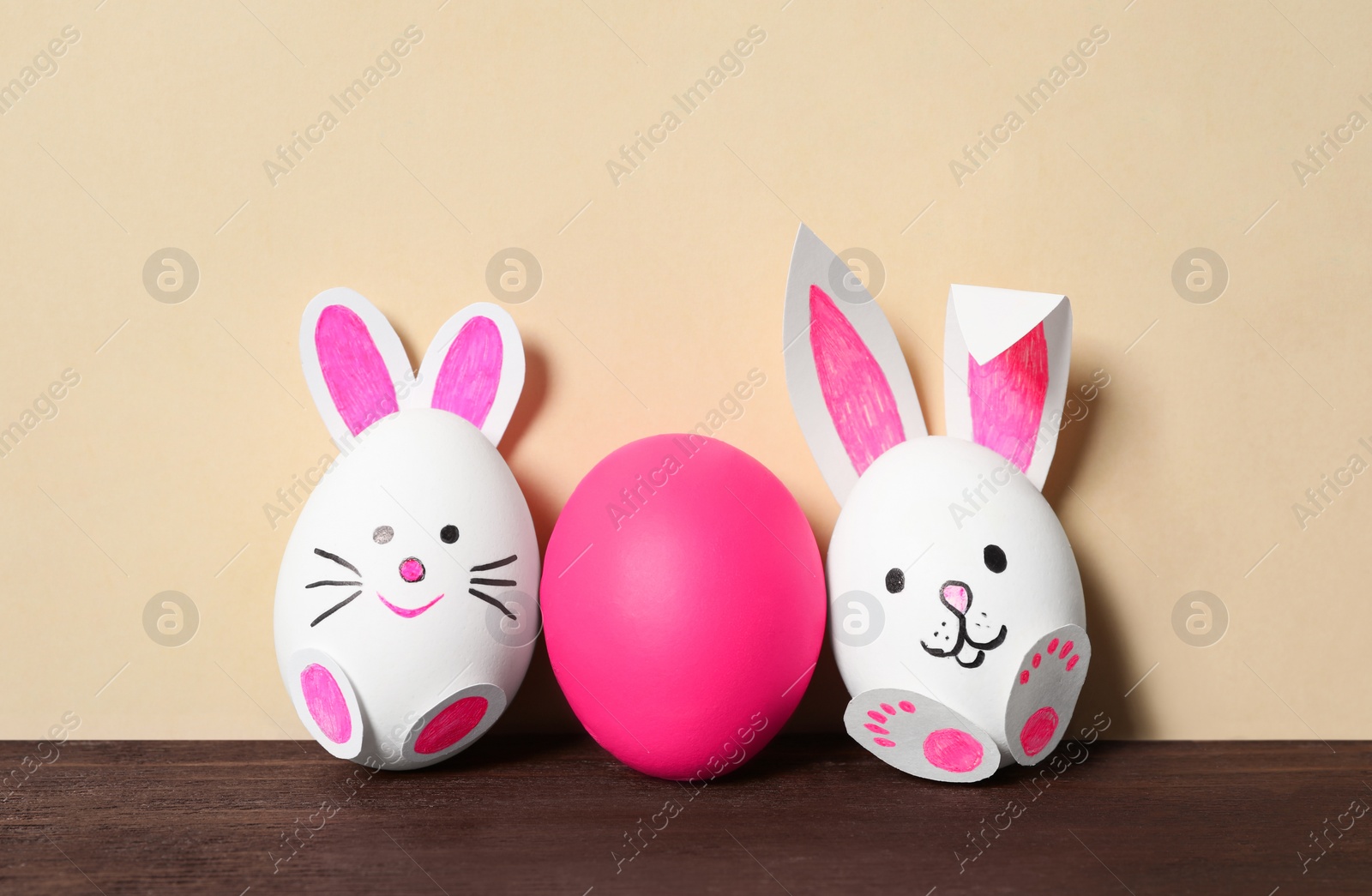 Photo of Eggs as cute bunnies and pink one on wooden table against beige background. Easter celebration