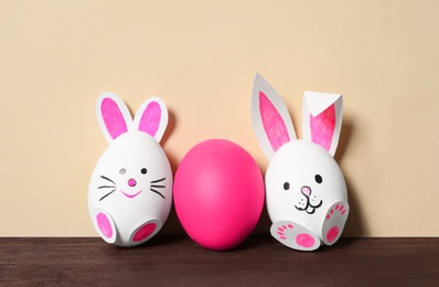 Photo of Eggs as cute bunnies and pink one on wooden table against beige background. Easter celebration
