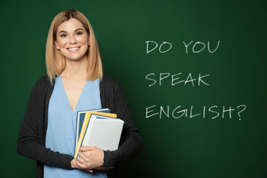 Beautiful teacher near green chalkboard with text Do You Speak English