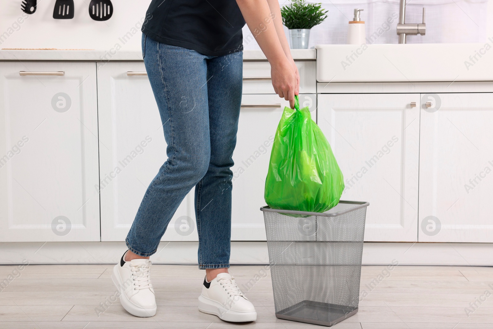 Photo of Woman taking garbage bag out of trash bin in kitchen, closeup