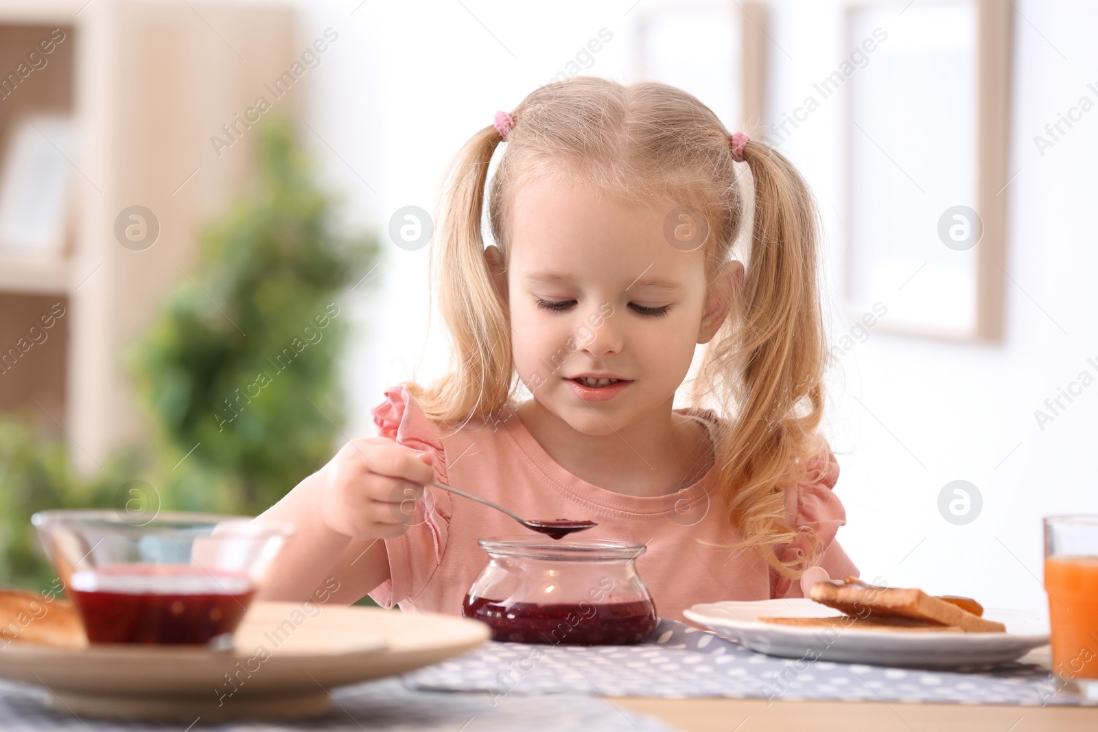 Photo of Cute little girl with jam and tasty toasted bread at table