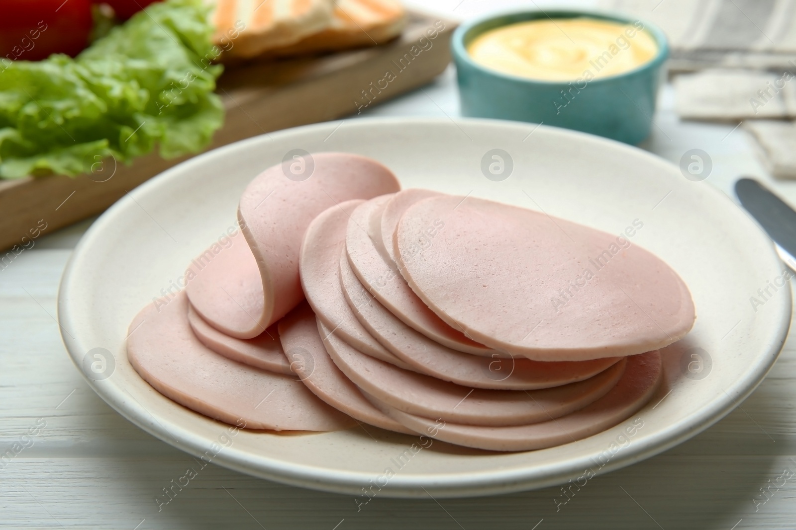 Photo of Slices of delicious boiled sausage on white wooden table, closeup