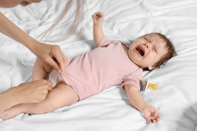 Mother putting clothes on crying daughter on bed