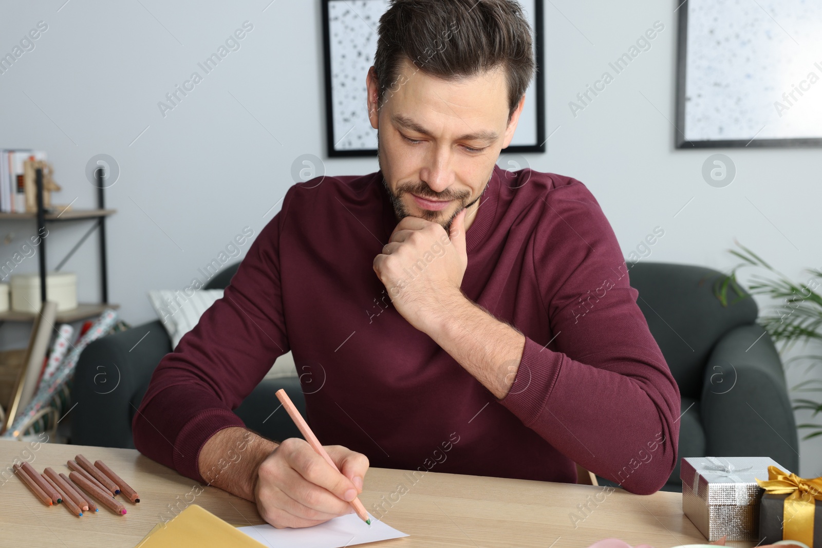 Photo of Man writing message in greeting card at wooden table in room