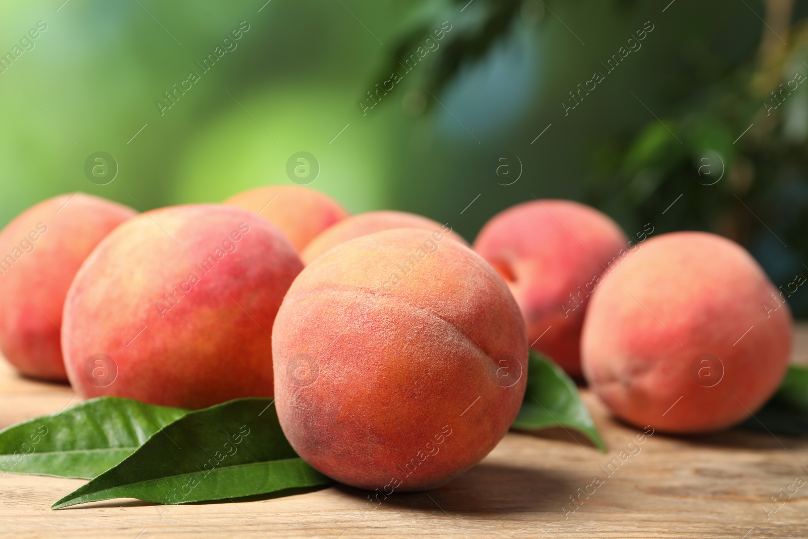 Photo of Fresh peaches and leaves on wooden table against blurred background, closeup