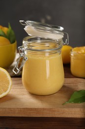 Photo of Delicious lemon curd in glass jars, fresh citrus fruit and green leaf on wooden table