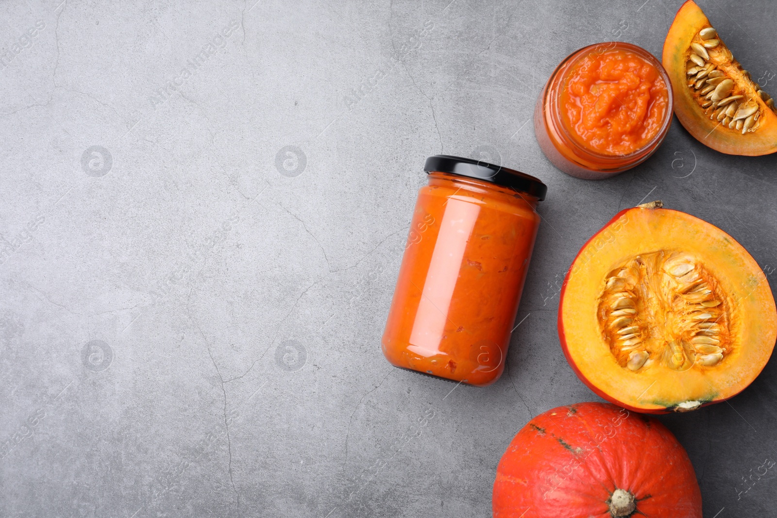 Photo of Jars of pumpkin jam and fresh pumpkins on grey table, flat lay. Space for text