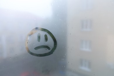 Sad face drawn on foggy window, space for text. Rainy weather