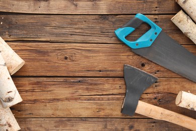 Photo of Saw with light blue handle, axe and firewood on wooden background, flat lay. Space for text