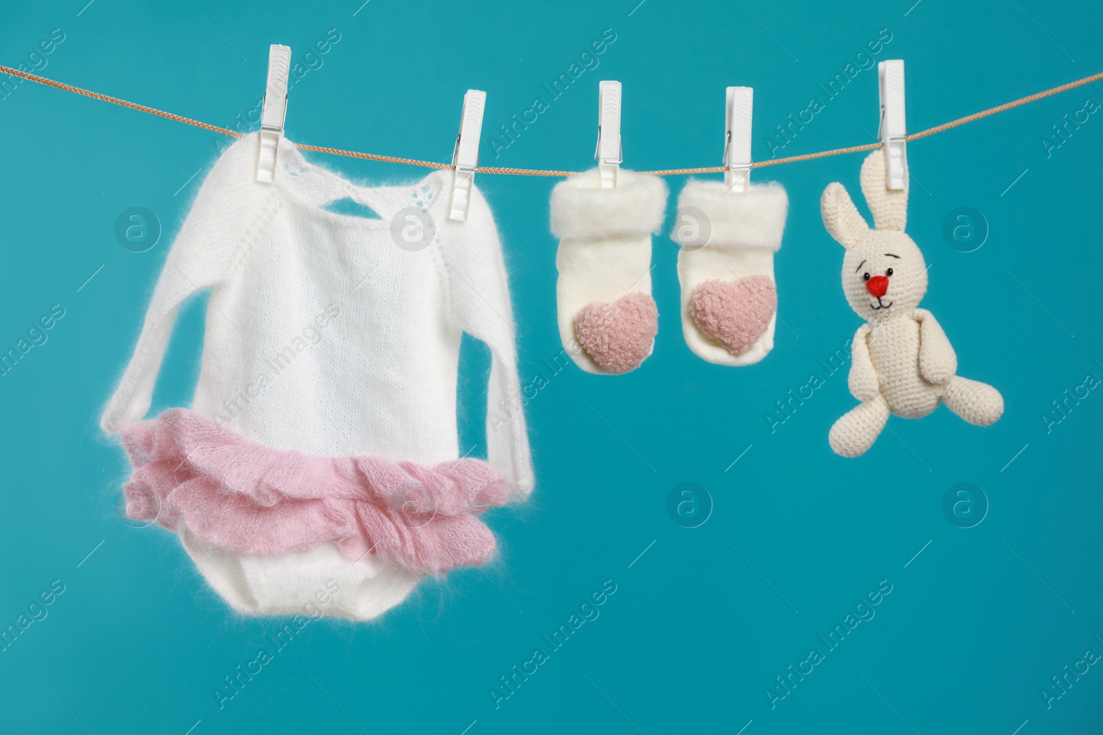 Photo of Knitted baby clothes and handmade toy drying on washing line against turquoise background