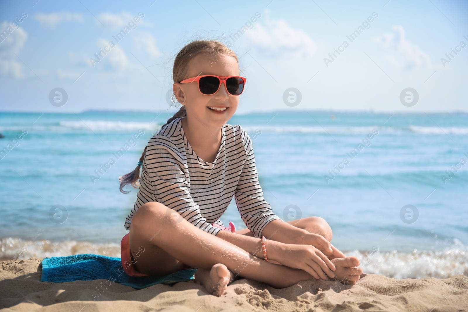 Photo of Happy little girl in stylish sunglasses on sandy beach near sea