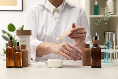 Photo of Dermatologist testing cosmetic product at light marble table indoors, closeup