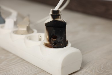 Photo of Burnt plug in power strip indoors, closeup. Electrical short circuit